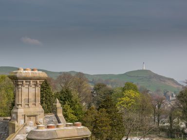A rooftop chimney with multiple pots and a hilly landscape with a tall monument on a hill in the background at The Alfred Suite Stone Cross Mansion in Ulverston