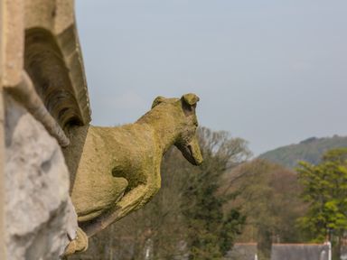 A stone dog sculpture on a building ledge overlooking trees and distant hills at The Alfred Suite Stone Cross Mansion in Ulverston