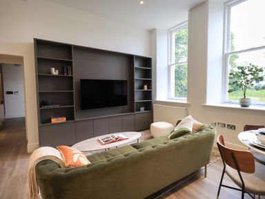 A living room with a green sofa a coffee table and a built-in shelving unit with a TV at The Alfred Suite Stone Cross Mansion in Ulverston