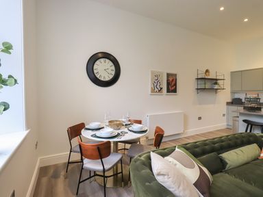 A dining area with a round table set with plates and glasses and wooden chairs next to a green sofa at The Alfred Suite Stone Cross Mansion in Ulverston