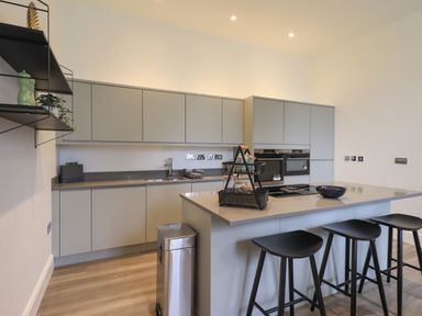 A kitchen with grey cabinets a countertop island with stools and appliances at The Alfred Suite Stone Cross Mansion Ulverston