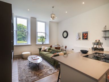A living room with green sofa round coffee table dining table and kitchen island with stove at The Alfred Suite Stone Cross Mansion in Ulverston
