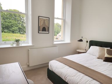 A bedroom with a bed beside two windows and a desk with a plant on it at The Alfred Suite Stone Cross Mansion in Ulverston