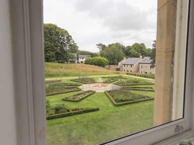 A garden with a geometric hedge design and a fountain viewed through a window at The Alfred Suite Stone Cross Mansion in Ulverston