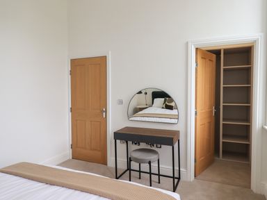 A bedroom with a wooden door a desk with a half round mirror a stool and an open closet with shelves at The Alfred Suite Stone Cross Mansion in Ulverston
