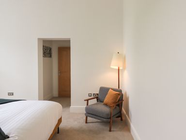 A bedroom with a bed, a gray armchair with an orange pillow, and a floor lamp at The Alfred Suite Stone Cross Mansion in Ulverston