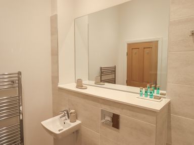 A bathroom with a sink mirror towel rack and toiletry bottles at The Alfred Suite Stone Cross Mansion in Ulverston
