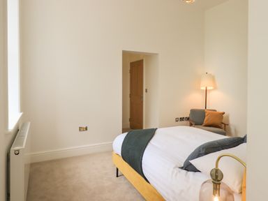 A bedroom with a bed a chair a floor lamp and a wooden door at The Alfred Suite Stone Cross Mansion in Ulverston