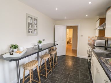 A kitchen with bar stools and a breakfast bar and a view of a bathroom through an open door at The Wheat House in Welford-On-Avon
