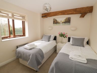 A bedroom with two single beds with grey blankets and pillows separated by a nightstand with flowers at The Wheat House in Welford-On-Avon