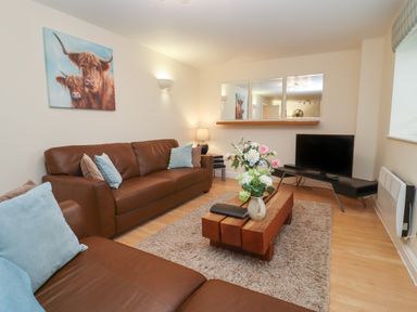 A living room with brown sofas a wooden coffee table with flowers a television and a painting of cows at The Wheat House in Welford-On-Avon