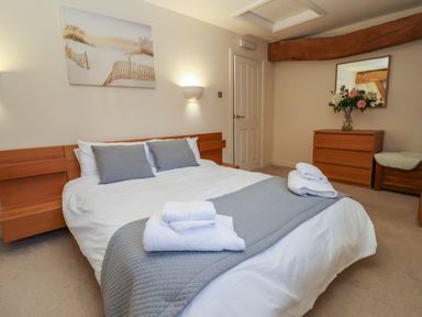 A bedroom with a double bed gray pillows and towels a wooden dresser and wall mirror at The Wheat House in Welford-On-Avon