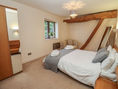 A bedroom with a bed pillows a chair mirror and wooden beams at The Wheat House in Welford-On-Avon