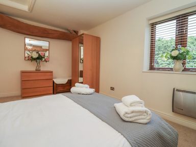 A bedroom with a bed with folded towels a wooden dresser a mirror a wardrobe a window with blinds and flowers on the windowsill at The Wheat House in Welford-On-Avon