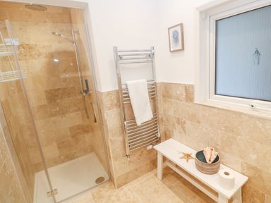 A bathroom with a shower enclosure towel rack bench with seashells and a frosted window at Alpha in St Minver