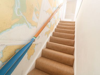 A stairway with a patterned carpet a wooden handrail made from a painted oar and a map on the wall at Alpha in St Minver