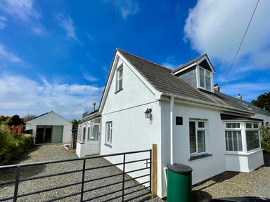 A white house with a pitched roof and detached garage on a gravel driveway at Alpha in St Minver