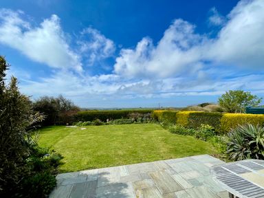 A garden with a lawn and hedges under a blue sky at Alpha in St Minver