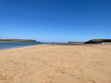 A wide sandy beach with footprints and water on the left and hills in the background at Alpha in St Minver