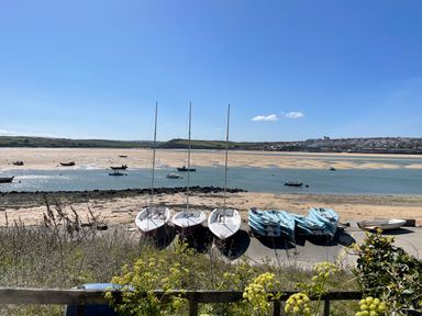 A coastal area with sailboats and kayaks on the shore with water and a distant town at Alpha in St Minver
