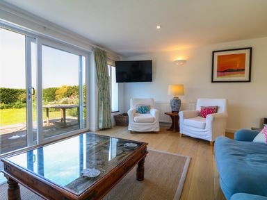 A living room with two white armchairs a blue sofa a wooden coffee table and sliding glass doors at Alpha in St Minver