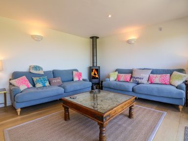 A living room with two blue sofas and a wood stove in the corner at Alpha in St Minver