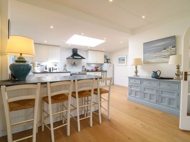 A kitchen with a breakfast bar with four chairs and a sideboard with two lamps and artwork at Alpha in St Minver