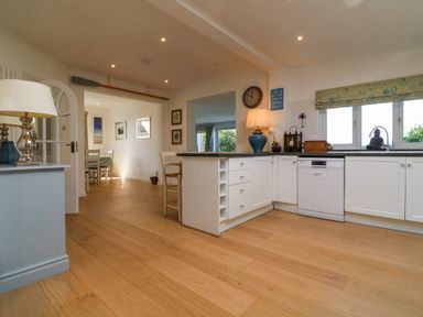 A kitchen with white cabinets dishwasher and wooden floor at Alpha in St Minver