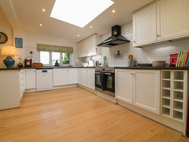 A kitchen with white cabinets a stove dishwasher and wooden floor at Alpha in St Minver