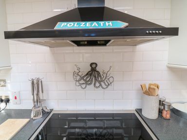 A kitchen stovetop with a black range hood with a polzeath sign and an octopus tile on white subway tile at Alpha in St Minver