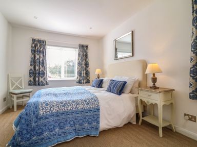A bedroom with a double bed blue patterned bedspread bedside table with lamp window with blue patterned curtains and a chair at Alpha in St Minver