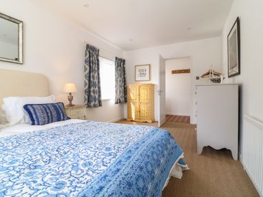 A bedroom with a double bed covered in blue and white bedding near window with blue patterned curtains at Alpha in St Minver