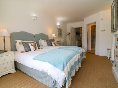 A bedroom with twin beds lamps and an open door leading to a bathroom at Alpha in St Minver