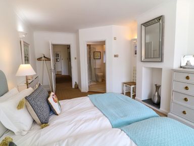 A bedroom with a bed a chair a dresser and a door to a bathroom at Alpha in St Minver