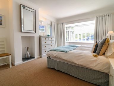 A bedroom with a bed next to a window with curtains a chest of drawers and a wall mirror at Alpha in St Minver