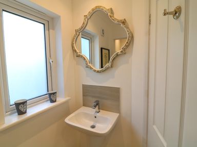 A bathroom with a decorative mirror above a sink and two cups on the window sill at Alpha in St Minver