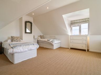 A bedroom with two single beds a mirror above a nightstand and a chest of drawers below a window at Alpha in St Minver