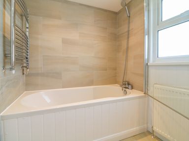 A bathroom with a bathtub a showerhead a towel radiator a window and a radiator at Alpha in St Minver