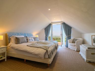 A bedroom with a bed armchair and chest by glass doors with curtains at Alpha in St Minver