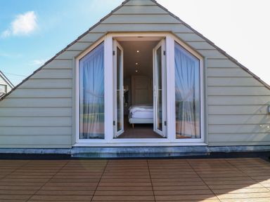 A bedroom visible through open glass doors on a balcony with wooden flooring at Alpha in St Minver