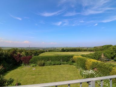 A garden with green grass bushes and flowers overlooking fields and a blue sky at Alpha in St Minver