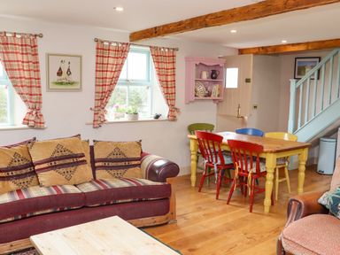A living room with a patterned sofa red and yellow chairs around a wooden table and a pink wall shelf at Cob Cottage in Kilmore County Wexford