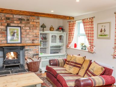A living room with a brick fireplace a red and patterned sofa a white cabinet and plaid curtains at Cob Cottage in Kilmore County Wexford