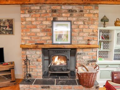 A brick fireplace with a wood burning stove and a basket of firewood in a living room at Cob Cottage in Kilmore County Wexford