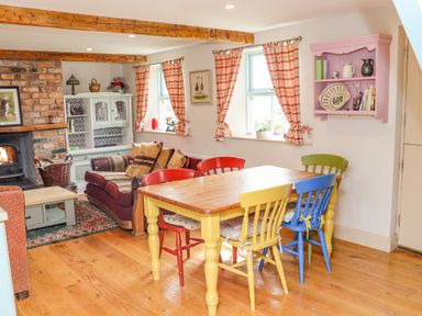 A dining area with a wooden table and colorful chairs next to a sitting area with a sofa and a fireplace at Cob Cottage Kilmore County Wexford