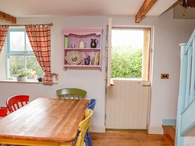 A dining area with a wooden table and colorful chairs next to a window with plaid curtains and an open half door at Cob Cottage Kilmore County Wexford