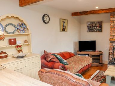 A living room with a red sofa a TV on a wooden stand a cream cabinet with plates and a clock on the wall at Cob Cottage in Kilmore County Wexford