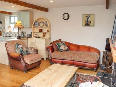 A living room with a leather armchair and sofa a wooden coffee table and a white cabinet at Cob Cottage Kilmore County Wexford
