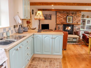A kitchen with light blue cabinets and wooden countertops next to a living room with a brick fireplace and wooden beams at Cob Cottage in Kilmore County Wexford