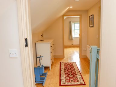 A hallway with wooden floor and a red patterned rug next to a blue rocking horse and a white chest of drawers at Cob Cottage in Kilmore County Wexford
